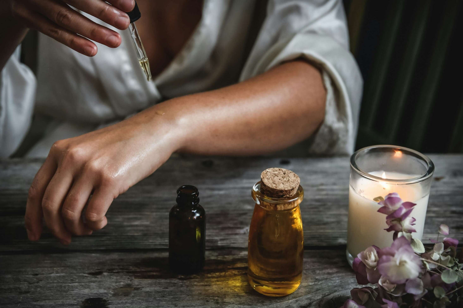 Essential oils and a candle on a rustic table, embodying relaxation and wellness in a serene home setting.